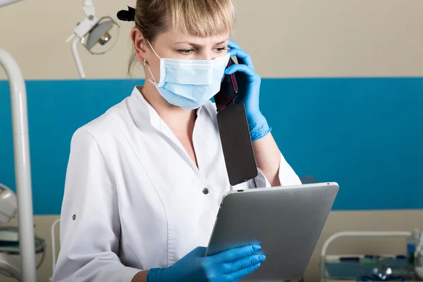 Mujer dentista llamar por teléfono y leer algo en la tableta de la PC. en el fondo del equipo dental — Foto de Stock