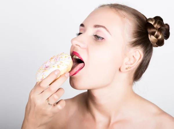 Девушка в ярком макияже ест вкусный пончик с глазурью. Смешная радостная женщина со сладостями, десертом. Концепция диеты. фастфуд. Девушка с нежностью смотрит на пончик — стоковое фото