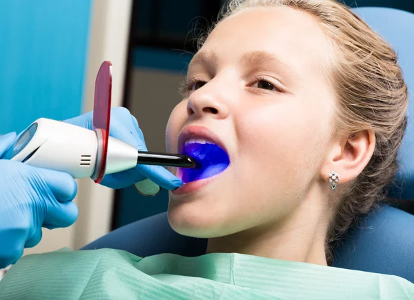 Niña feliz con la boca abierta sometida a tratamiento dental en la clínica. El dentista revisó y curó los dientes de un niño paciente en el consultorio dental — Foto de Stock