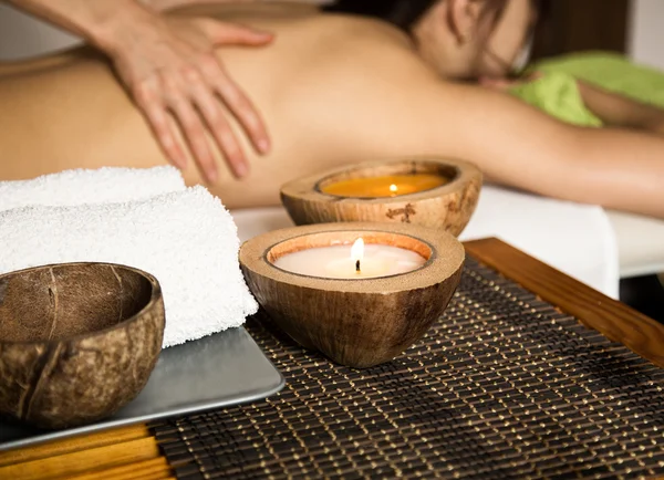 Mujer joven recibiendo un masaje de espalda en el salón de spa. primer plano de una vela y toallas — Foto de Stock