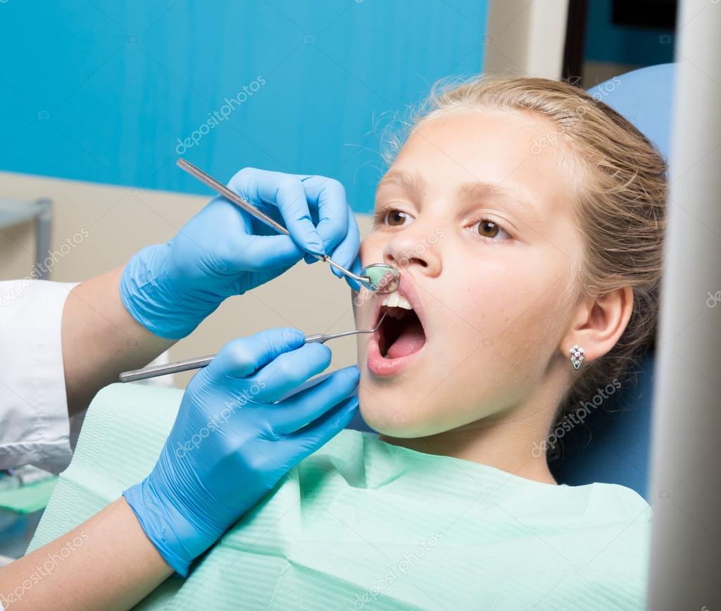 Happy little girl with open mouth undergoing dental treatment at clinic