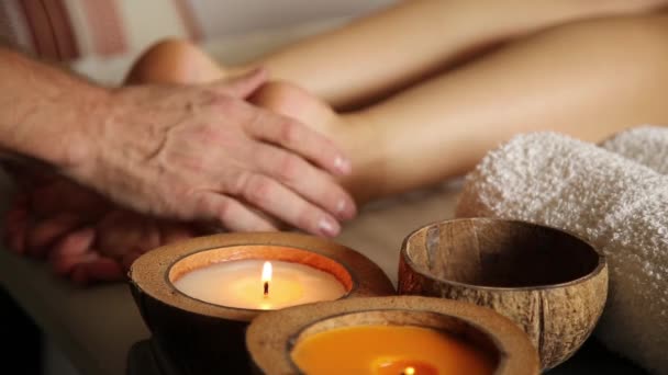 Mujer joven recibe un masaje de pies en el salón de spa. primer plano de las velas. manos masculinas se deslizan sobre las piernas femeninas — Vídeos de Stock
