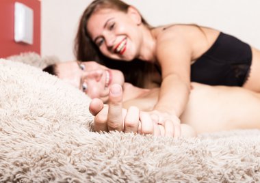 Seksi genç çift öpüşme ve yatakta oynuyor. ellerin yakın çekim ve şişkin orta parmak