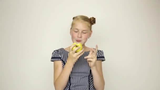 Красива молода дівчина, одягнена в смугасту сукню, їсть яблуко. здорова їжа - концепція міцних зубів — стокове відео