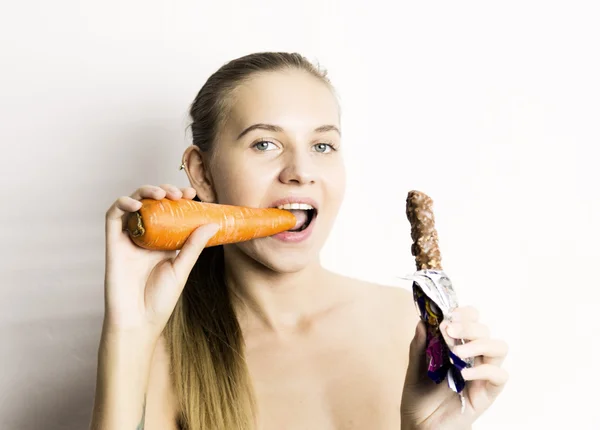 Hermosa mujer joven desnuda comiendo una zanahoria. zanahoria vs chocolate. comida saludable - concepto de dientes fuertes — Foto de Stock