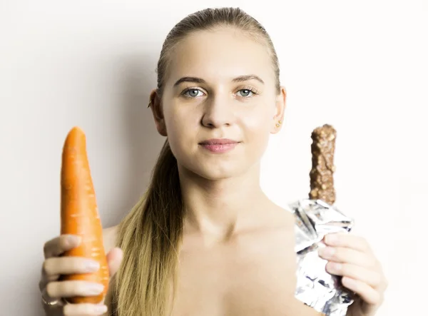 美しい裸若い女性は、ニンジンを食べるします。ニンジン vs チョコレート。健康食品 - 強力な歯のコンセプト — ストック写真