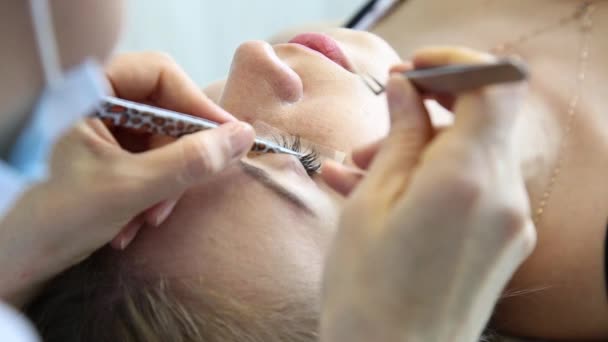 Schöne junge Frau mit Wimpernverlängerung. Frauenauge mit langen Wimpern. Kosmetikerin Wimpernverlängerung für junge Frau im Schönheitssalon — Stockvideo