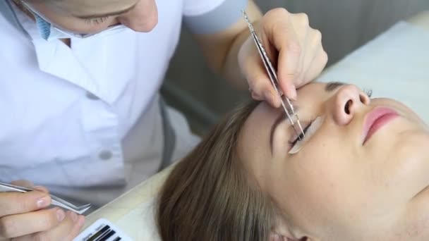 Mooie jonge vrouw met wimper extensie. De ogen van de vrouw met lange wimpers. Schoonheidsspecialiste wimper uitbreiding voor jonge vrouw in een schoonheidssalon — Stockvideo