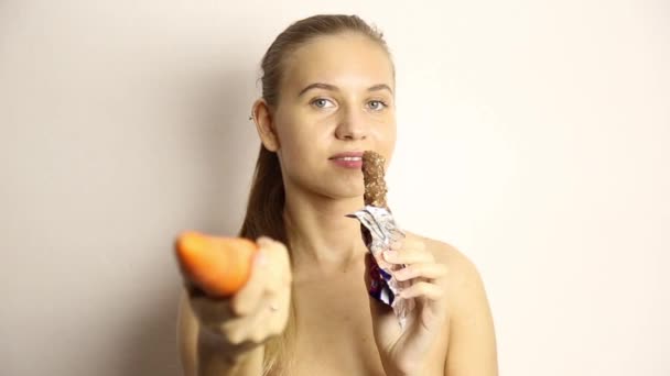 Belle jeune femme nue mangeant une carotte. carotte vs chocolat. aliments sains - concept de dents fortes — Video