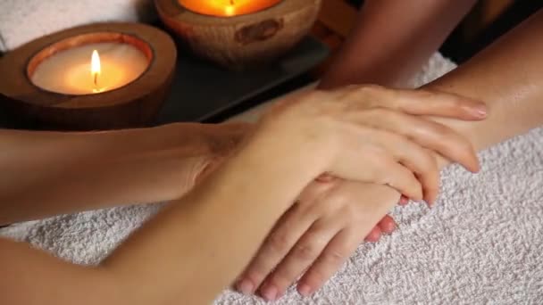 Jovem recebe uma massagem na mão no salão de spa. close-up de velas. braços massagista deslizar na mão feminina — Vídeo de Stock