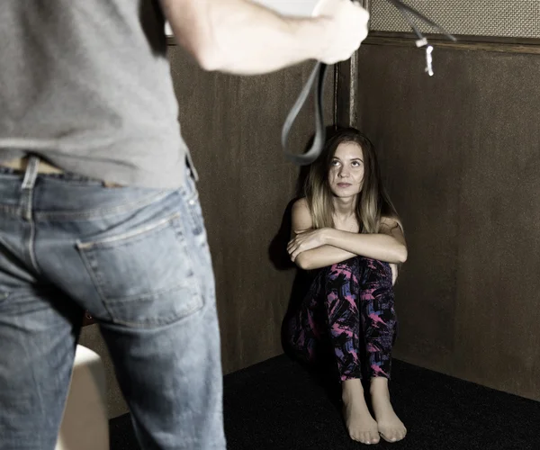 Mujer asustada sentada en la esquina con un hombre sin rostro sosteniendo un cinturón, una sesión conceptual que retrata el proceso y los efectos de la violencia doméstica —  Fotos de Stock