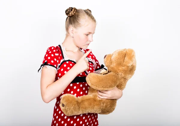 Schöne junge Mädchen in einem roten Kleid mit weißen Tupfen hält einen Teddybär gekleidet — Stockfoto