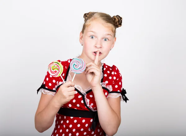 Porträt eines glücklichen schönen jungen Mädchens mit süßen Bonbons. hübsche junge Frau in einem roten Kleid mit weißen Tupfen und zwei bunten Lutschern — Stockfoto