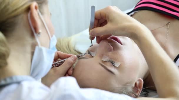 Belle jeune femme avec extension de cils. Œil de femme avec de longs cils. Extension de cils esthéticienne pour jeune femme dans un salon de beauté — Video