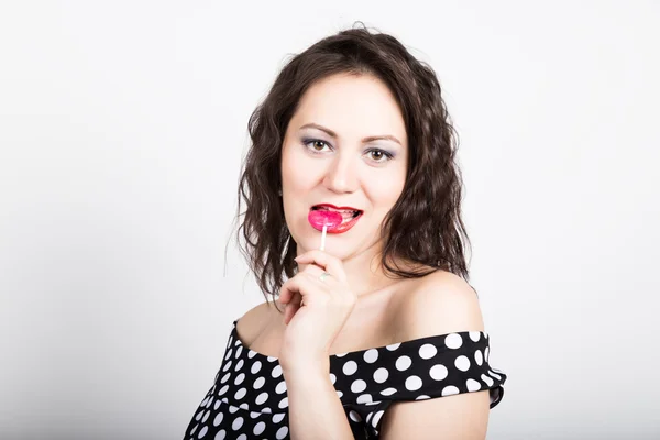 Retrato de feliz hermosa joven lamiendo dulces dulces y expresando diferentes emociones. bonita mujer con corazón en forma de piruleta — Foto de Stock