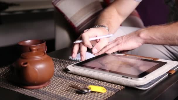 Jeune homme d'affaires utilisant un ordinateur tablette pour faire des achats en ligne et prendre des notes dans un carnet. Homme travaillant sur pc tablette et boire du thé dans le café — Video