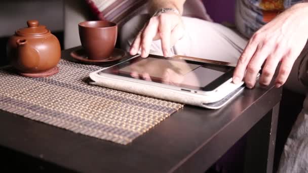 Jungunternehmer nutzt Tablet-Computer für Online-Einkäufe. Mann arbeitet an PC-Tablet und trinkt Tee im Café — Stockvideo