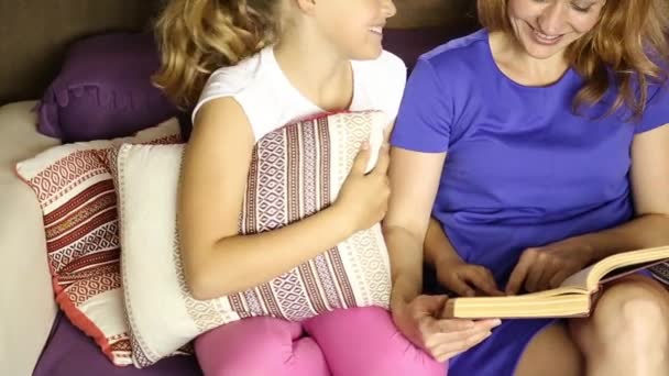 Joven mamá leyendo un libro en voz alta a su hija en la sala de estar en el sofá antes de dormir — Vídeos de Stock