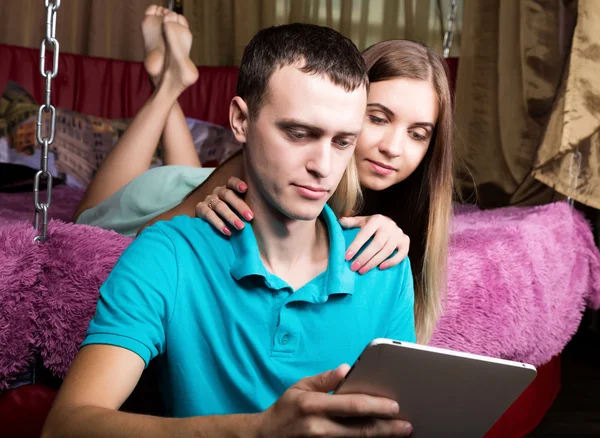 Tineri cuplu de cumpărături on-line folosind calculator comprimat digital. Cuplu râzând, fată întinsă pe pat acasă și tip așezat lângă podea — Fotografie, imagine de stoc