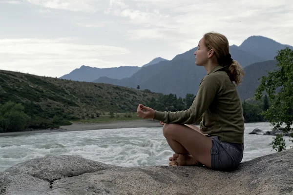 Mujer joven sentada en el borde del acantilado sobre el río de la montaña — Foto de Stock