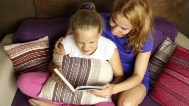 Bir kitap yüksek sesle kızı kanepeye oturma odasında uyumadan önce gönüllülük-e doğru genç anne