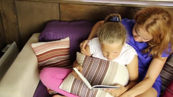 Ung mamma högläsning en bok till sin dotter i vardagsrummet på soffan innan sova — Stockvideo