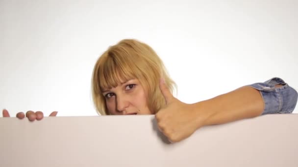 Ler glad kvinna står bakom och lutande på en vit tom billboard eller plakat, uttrycker olika känslor och visar tummen till toppen. över vit bakgrund — Stockvideo