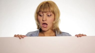 Gülümseyen mutlu kadın arkasında duran ve beyaz boş bir reklam panosu ya da pankart yaslanmış, kenarına bakarak ve bir pankart arkasına saklanıyor. beyaz arka plan üzerinde