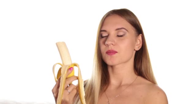 Jeune femme nue porte rouge à lèvres et a les cheveux vers le bas, et brossé, éplucher et manger une grande banane. aliments sains - concept de dents fortes. Sur fond blanc — Video