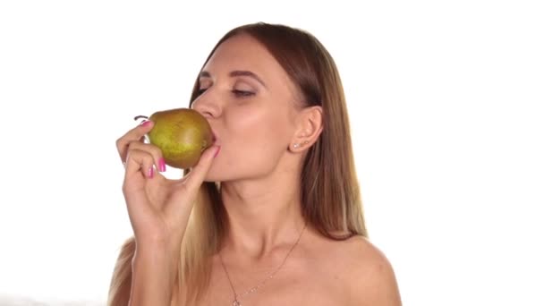 Naked young woman wears red lipstick and has her hair down, and brushed, eating a big, juicy pear. healthy food - strong teeth concept. On a white background — Stock Video