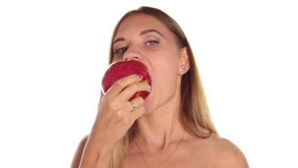 Mujer joven desnuda usa lápiz labial rojo y tiene el pelo suelto, y cepillado, comiendo una manzana grande, de color rojo oscuro. comida saludable - concepto de dientes fuertes. Sobre un fondo blanco — Vídeo de stock