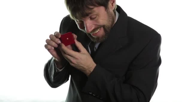 Hombre barbudo en un traje de negocios da un anillo en la caja roja y expresa diferentes emociones — Vídeo de stock