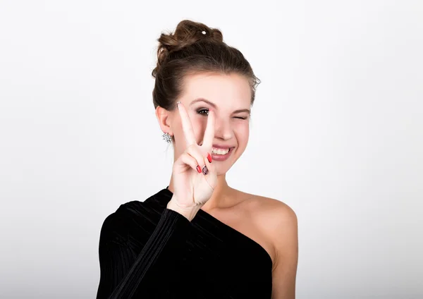 Foto de cerca de la moda joven en vestido negro elegante, mujer juguetona sonriendo y muestra un signo de paz — Foto de Stock