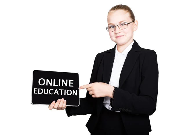 Hermosa chica de la escuela en un traje de negocios sostiene una tableta de PC en sus manos y mirando a la cámara, en una tableta de PC inscripción educación en línea —  Fotos de Stock