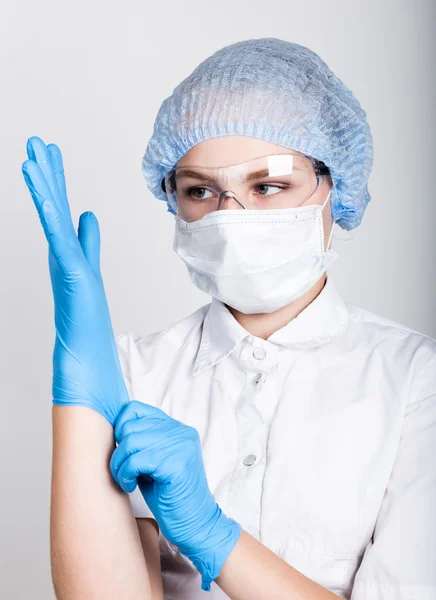 Маленька дівчинка, одягнена в медичний одяг, втягує в руки медичні рукавички — стокове фото