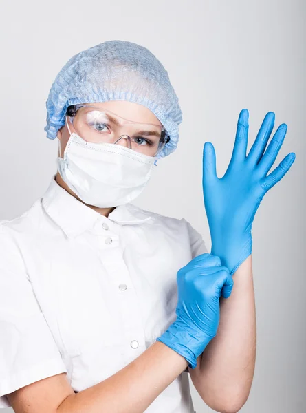 Маленька дівчинка, одягнена в медичний одяг, втягує в руки медичні рукавички — стокове фото