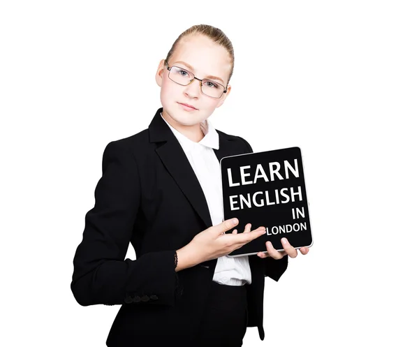 Hermosa chica de la escuela en un traje de negocios sostiene una tableta de PC en sus manos y mirando a la cámara, en una tableta de PC inscripción aprender inglés en Londres — Foto de Stock