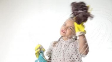 gülümseyen küçük ev hanımı bir sprey, bez ve deterjan ile pencereyi yıkadı. Köpük büyük cam. Ev işi konsepti.