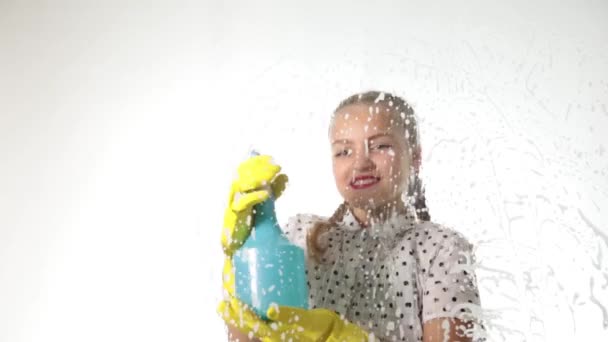 Une petite ménagère souriante a lavé la fenêtre avec un spray, un chiffon et un détergent. Grand verre en mousse. Concept de travaux ménagers . — Video