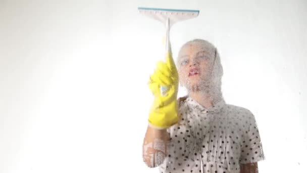 Glimlachend kleine huisvrouw gewassen het raam met een spray, doek en wasmiddel. Groot glas in schuim. Huiswerk concept. — Stockvideo
