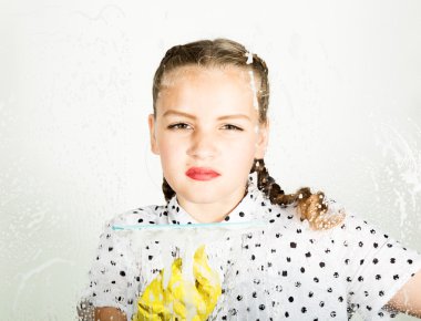 Küçük ev kadını gülümseyen bir bez ve deterjan ile pencere yıkanmış. Köpük büyük bardakta. Ev kavramı.