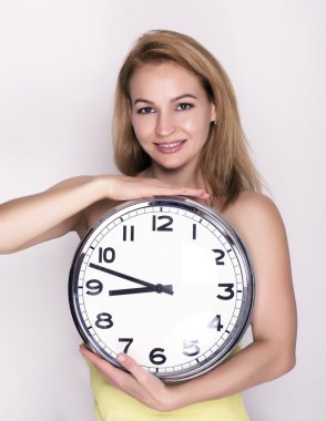 Beautiful young woman looking at a large silver retro clock that she is holding, she wonders how much time passed