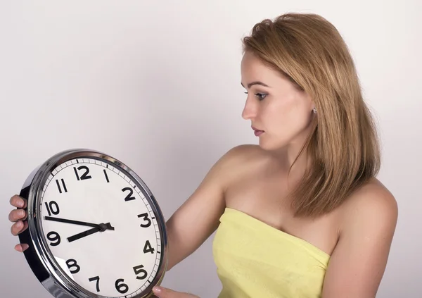 Beautiful young woman looking at a large silver retro clock that she is holding, she wonders how much time passed — Zdjęcie stockowe