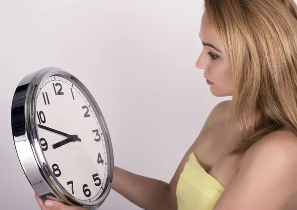 Beautiful young woman looking at a large silver retro clock that she is holding, she wonders how much time passed — Stockfoto