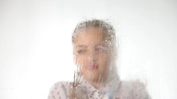 Close-up smiling little housewife washed the window with a spray, cloth and detergent. Large glass in foam. Housework concept. — Stock Video