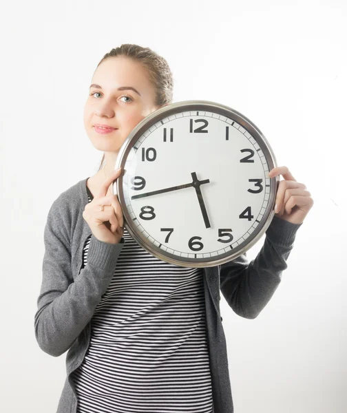 Beautiful young woman looking at a large silver retro clock that she is holding, she wonders how much time passed — ストック写真