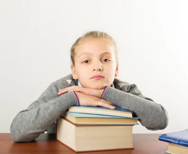 Adolescente sentada en una mesa frente a su gran pila de libros. colegiala leyendo un libro y haciendo la tarea — Foto de Stock
