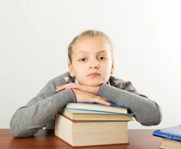 Adolescente sentada en una mesa frente a su gran pila de libros. colegiala leyendo un libro y haciendo la tarea —  Fotos de Stock