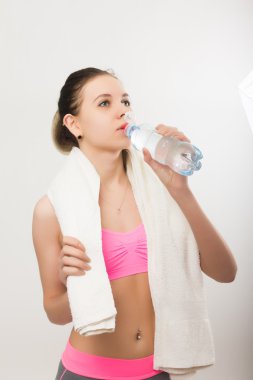 Young athletic girl finished training, holding a bath towel, drinks water from a bottle clipart