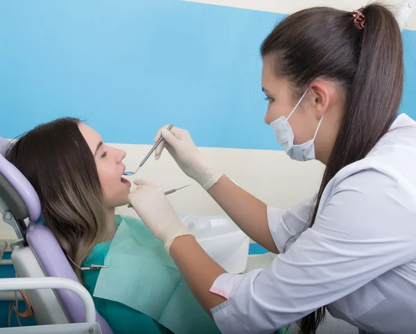 Jonge vrouw bezoeken tandarts in stomatological kliniek. Dokter onderzoekt de mondholte op tandbederf. — Stockfoto